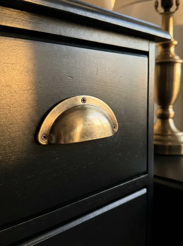 Brushed-brass drawer hardware adding warmth to a matte-black bedroom dresser.