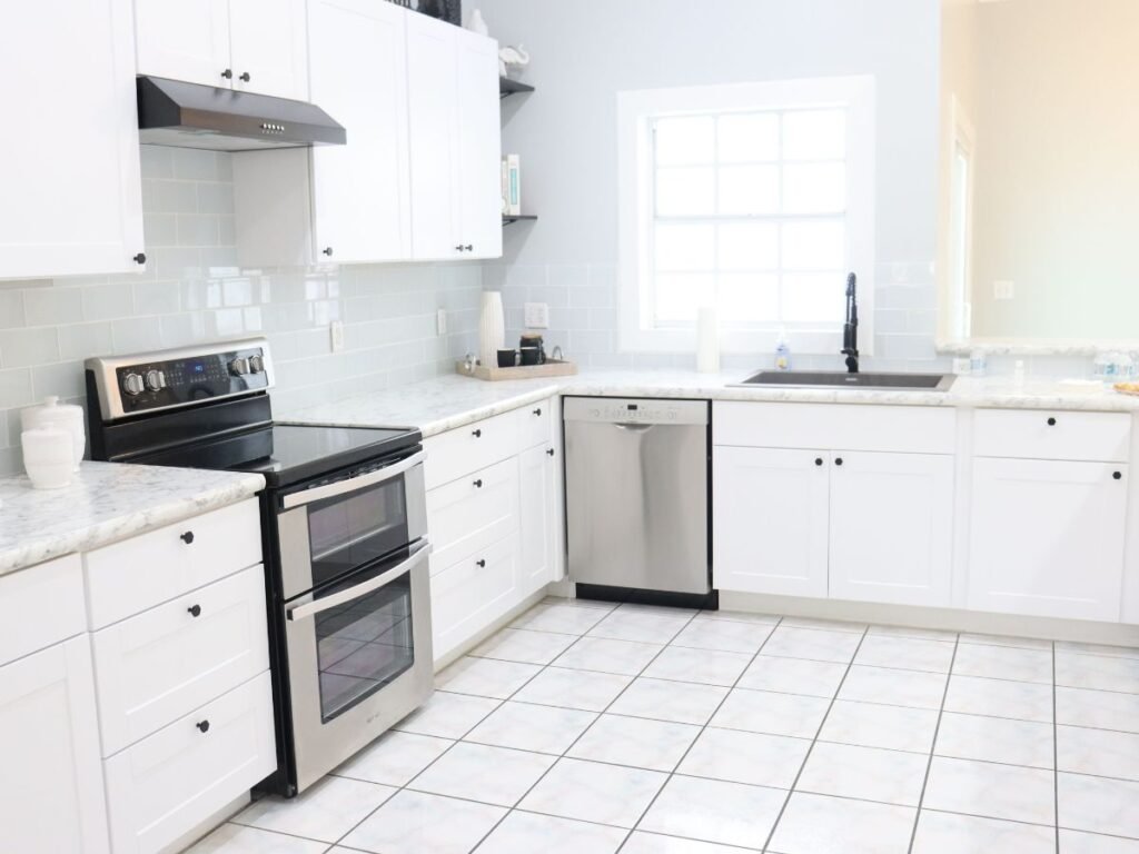 Bright white kitchen with black appliances, gray backsplash, and tiled flooring