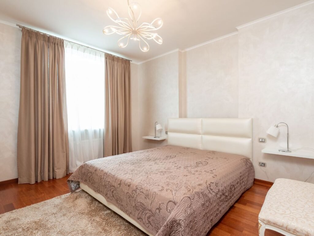 Neutral bedroom with a large bed, beige curtains, and warm wood flooring