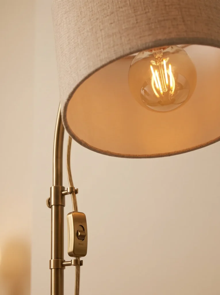 Warm 2700K LED bulb glowing beneath a linen shade beside a dimmer and managed cord.